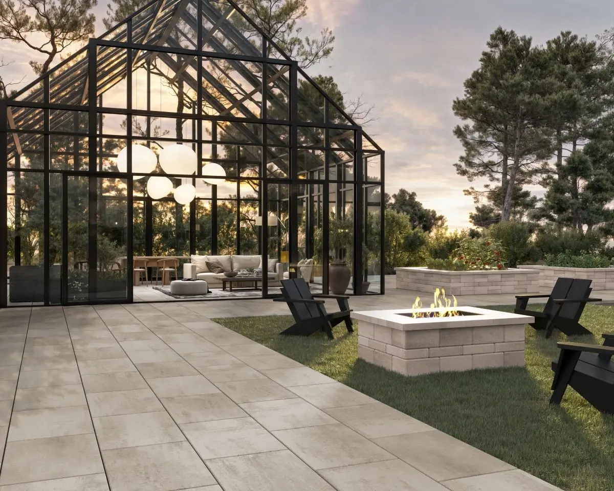 Terrasse élégante aménagée avec les dalles Industria 900x600 en teinte Caffè Crema, complétée par un foyer carré et une serre vitrée moderne pour une ambiance extérieure soignée
