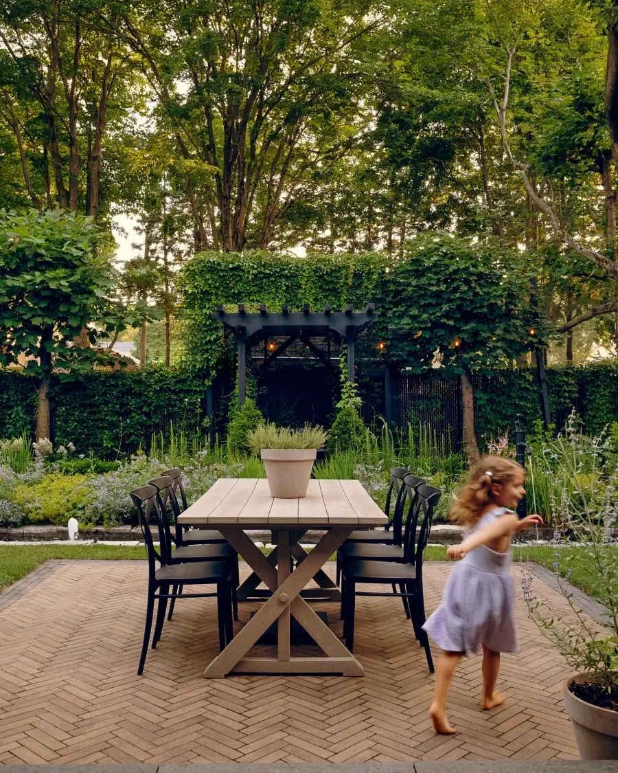 Terrasse arrière avec coin repas, pavés Techo-Bloc aux tons chauds en motif chevron et végétation luxuriante.
