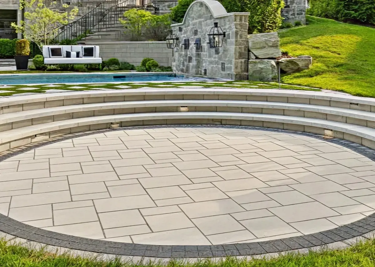Circular patio area prepared for fire pit installation, surrounded by tiered stone steps and a landscaped poolside setting.