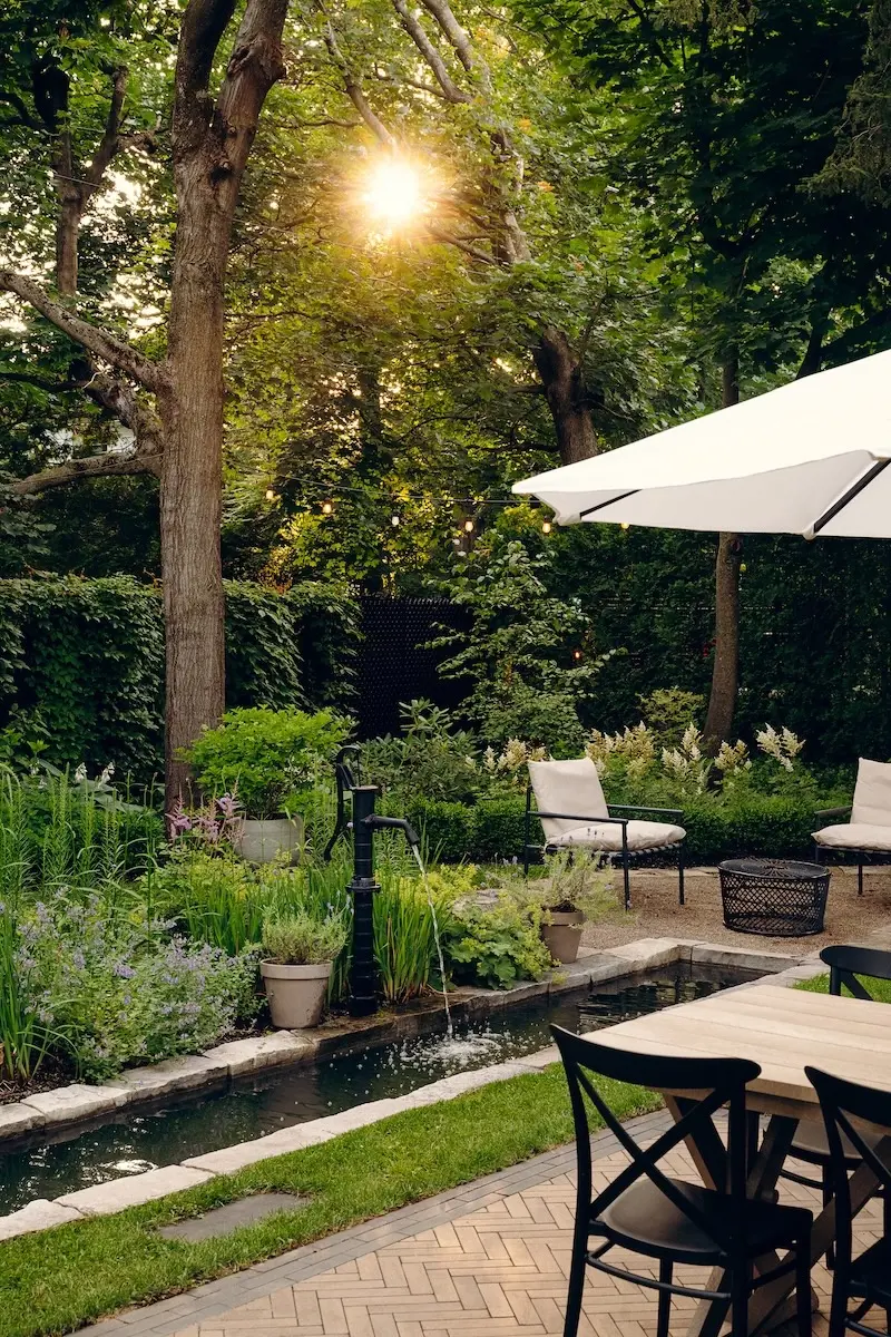 Shaded backyard dining area with Techo-Bloc Westmount pavers, Limestone cap edging, garden planting, umbrella, and warm evening light.