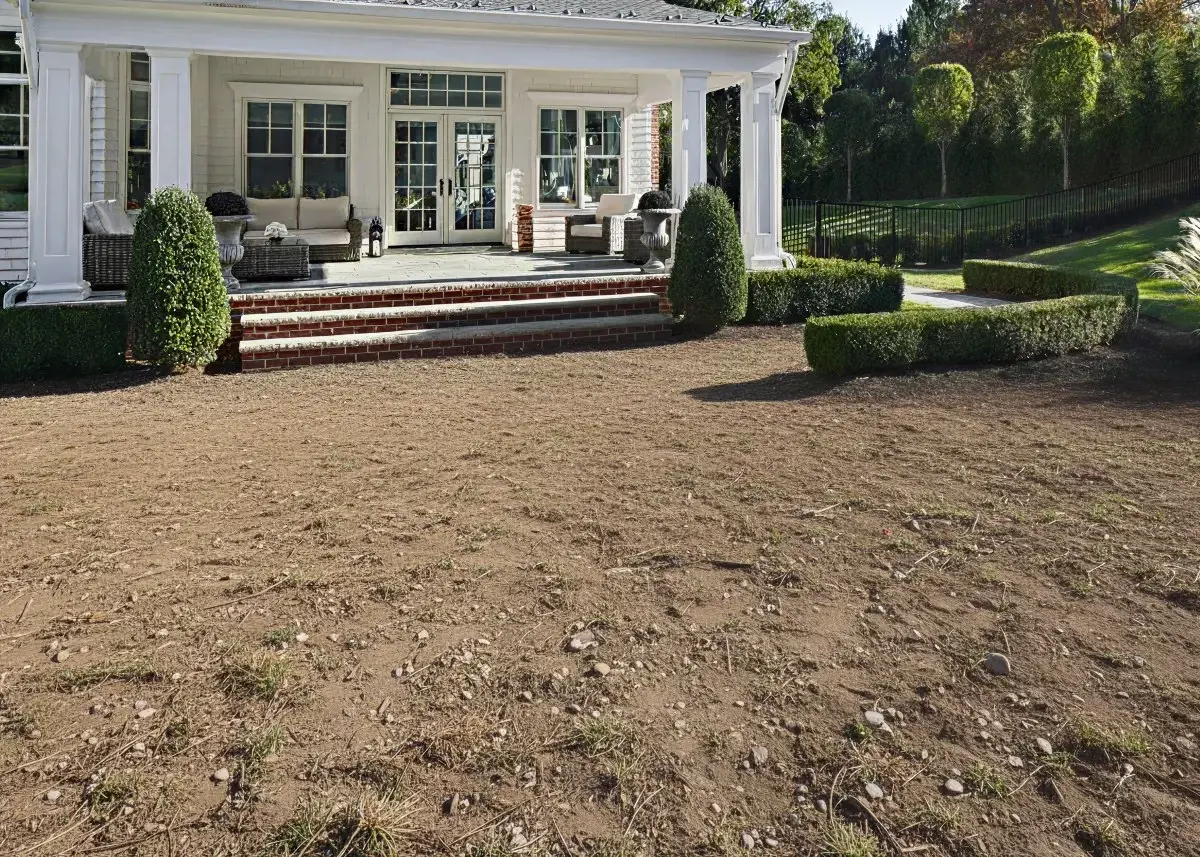 Backyard prepared for slab installation in front of a white covered patio with brick steps and trimmed hedges.