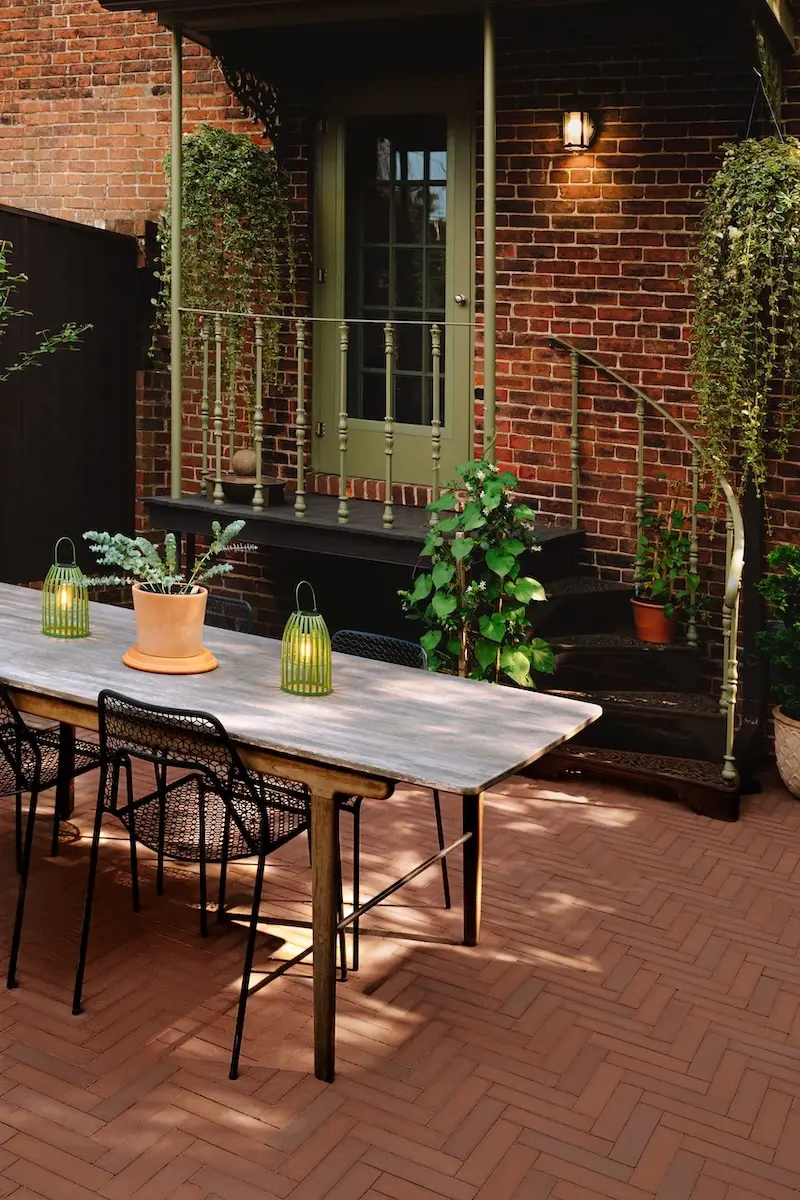 Coin repas extérieur dans une petite cour arrière en brique avec pavés Westmount de Techo-Bloc, table en bois, chaises, plantes et éclairage chaleureux.