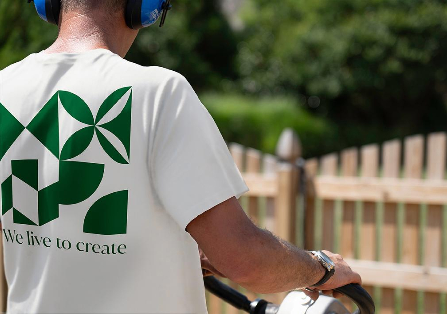 Back view of a person wearing a white co-branded Techo-Bloc t-shirt with a bold green geometric design and the phrase “We live to create.”