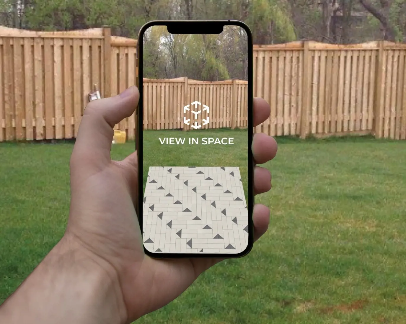 Hand holding a smartphone showing Techo-Bloc augmented reality preview of patio pavers on grass with “View in Space” text.