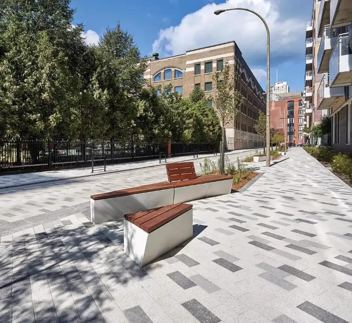 Urban walkway paved with Techo-Bloc pavers and lined with benches, trees, and surrounding buildings.