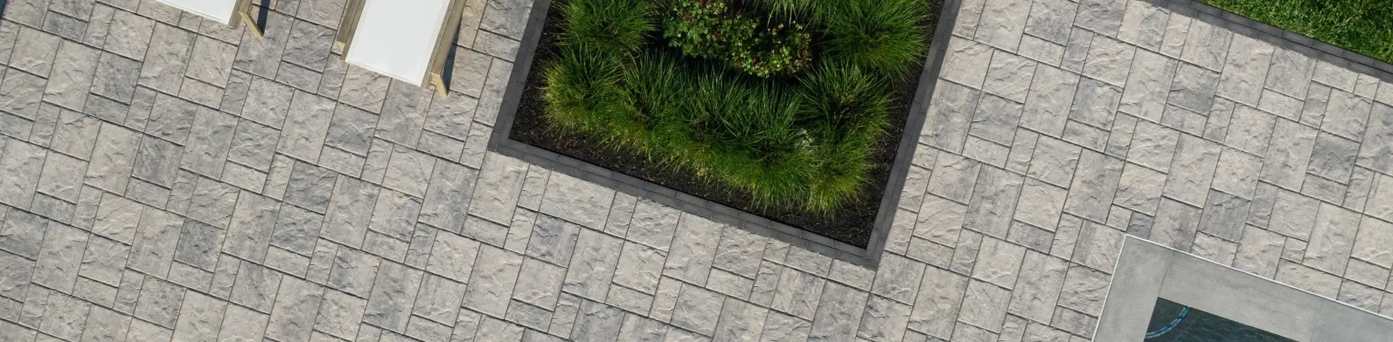 Blu 60 slab by Techo-Bloc in Shale Grey with slate texture, arranged in a modular pattern around a square garden inlay.