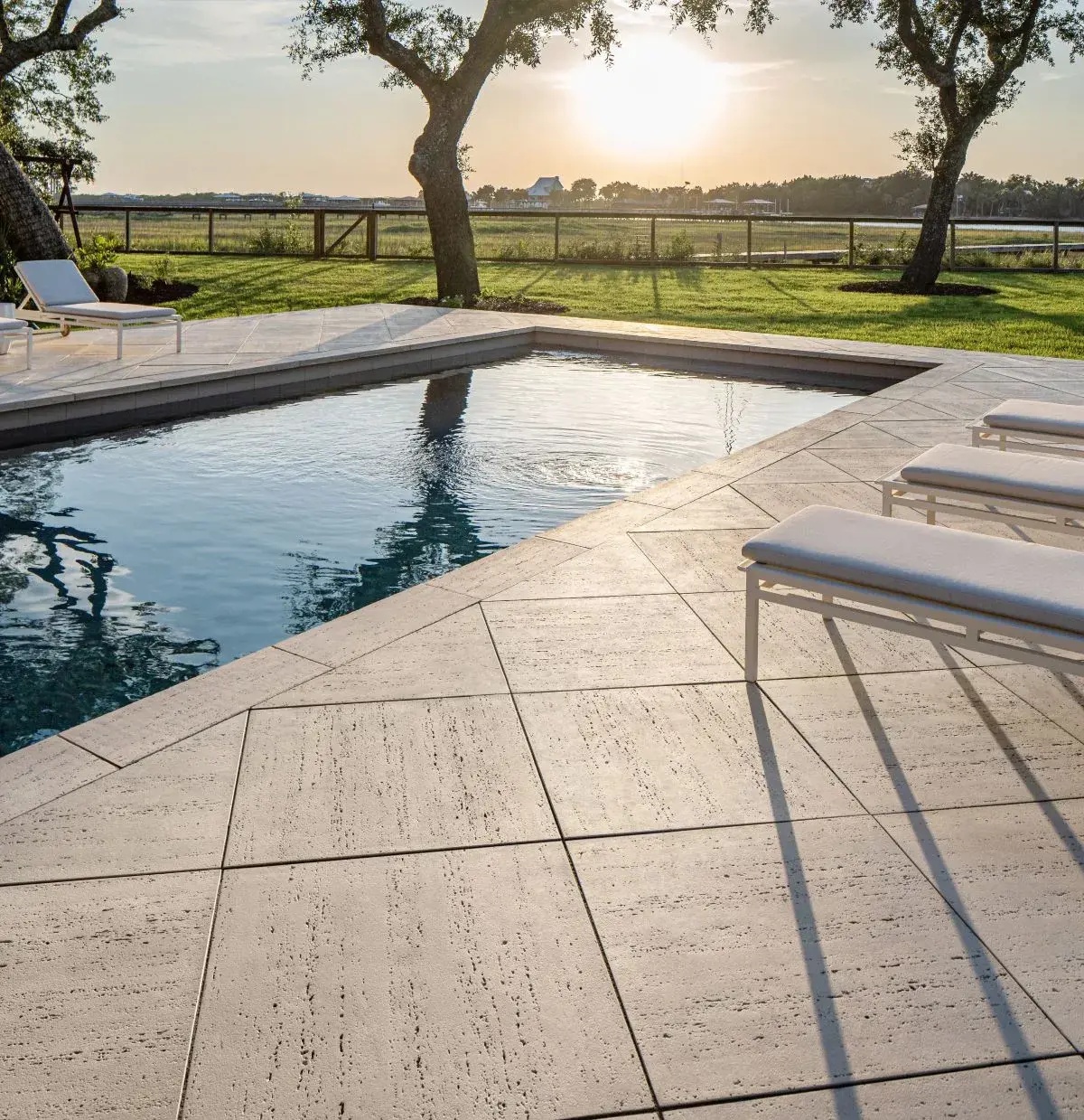 Un patio au bord de la piscine avec des chaises longues et une végétation luxuriante, avec une dalle brute en travertin ivoire pour un look élégant et moderne.