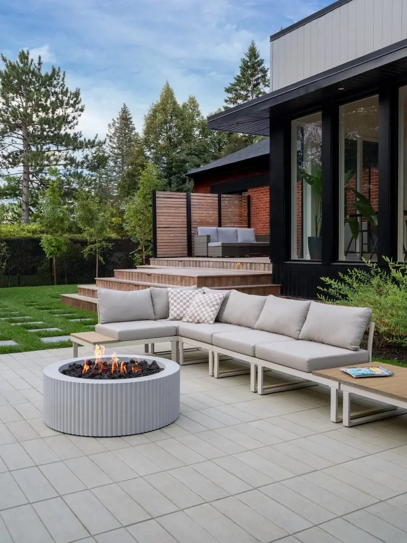 Backyard lounge patio with Techo-Bloc Industria pavers, outdoor sofa, round fire feature, Terrazzo slab accents, and modern home exterior.