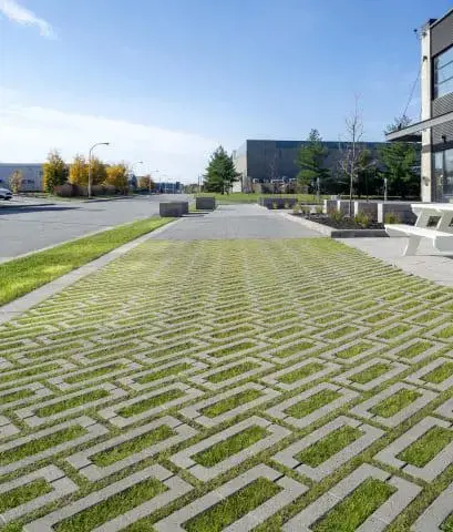 Permeable pavement system using Techo-Bloc commercial pavers arranged in a geometric pattern, allowing grass infiltration in an urban landscape.