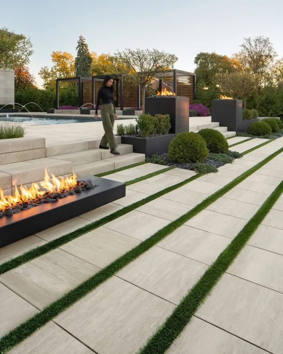 Stepped outdoor space featuring Industria Smooth Slabs in Caffè Crema with grass inlays and linear fire features, blending warmth with structure.