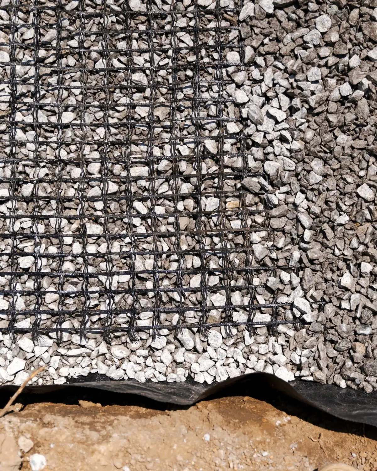 Geogrid mesh and gravel layers shown in a compacted paver base system for ground reinforcement.