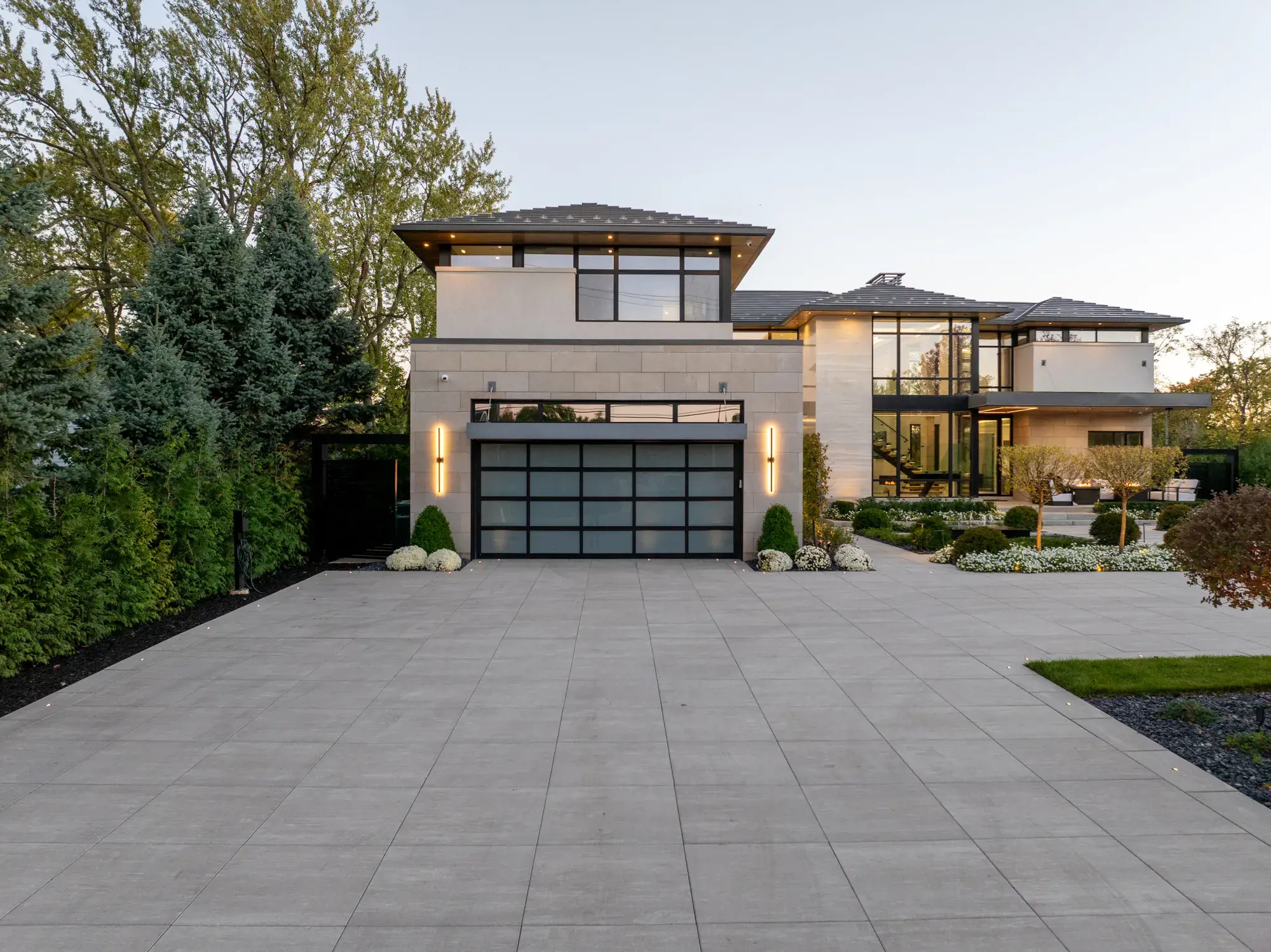 Façade de maison moderne au crépuscule avec porte de garage vitrée et entrée de cour Industria