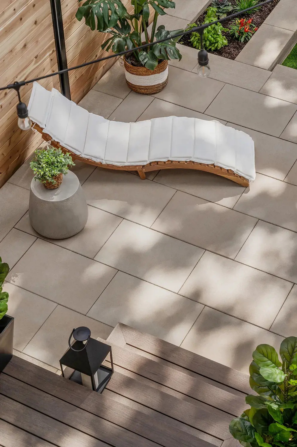Chaise longue à coussin blanc sur le patio de dalles, avec plante en pot et table d'appoint
