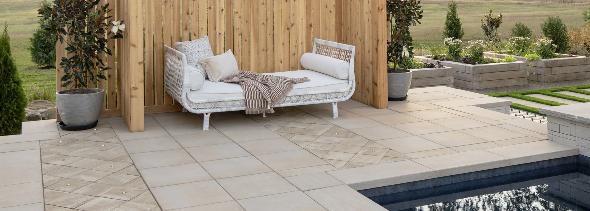 Modern backyard lounge featuring Ocean Grande slabs in Greyed Nickel, a wood privacy screen, cozy outdoor seating, and lush planting for a serene wellness retreat.