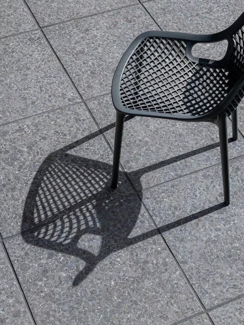 Close-up of Techo-Bloc Terrazzo slabs with an outdoor dining chair shadow on a modern backyard patio.