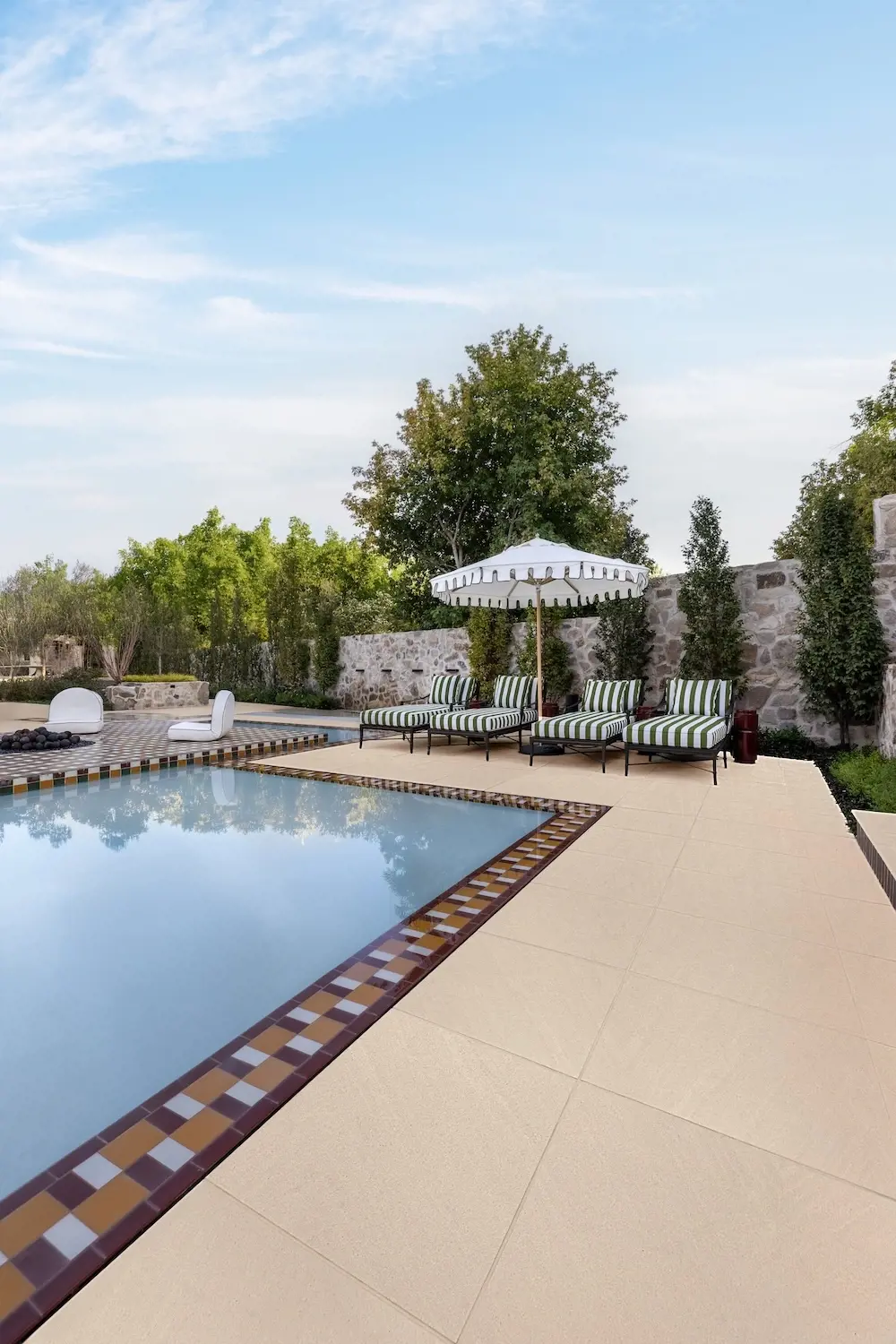 Refined backyard pool terrace with Techo-Bloc Sandstone slabs, lounge seating, umbrella, stone wall, and manicured greenery.