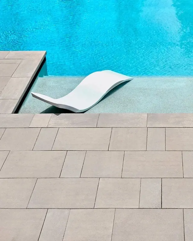 Patio moderne en pierre beige autour de la piscine avec siège relaxant dans l’eau.