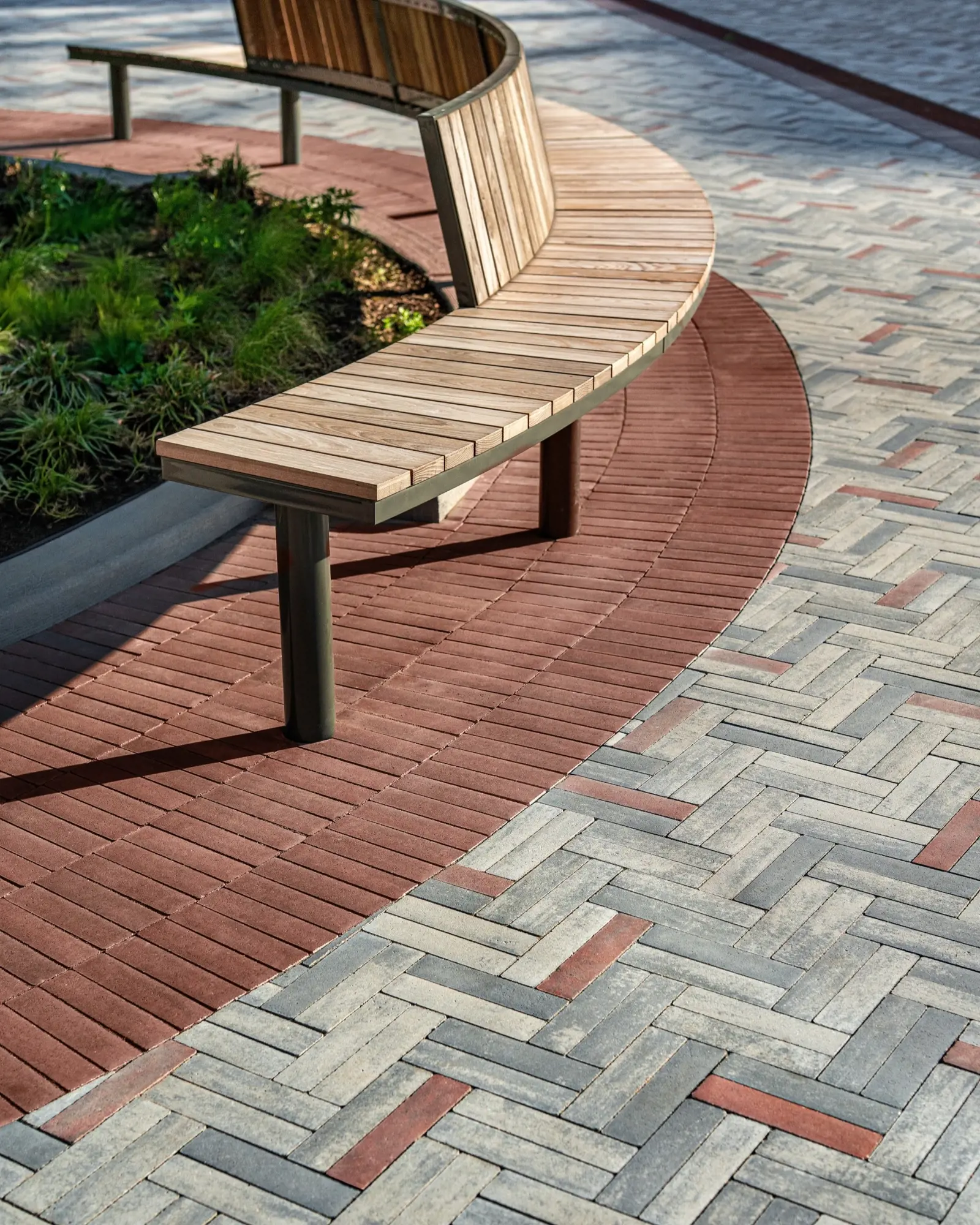 Banc en bois courbé installé au-dessus de pavés Westmount HD² Smooth contrastés en motif chevrons doubles rouge et gris au NJPAC.