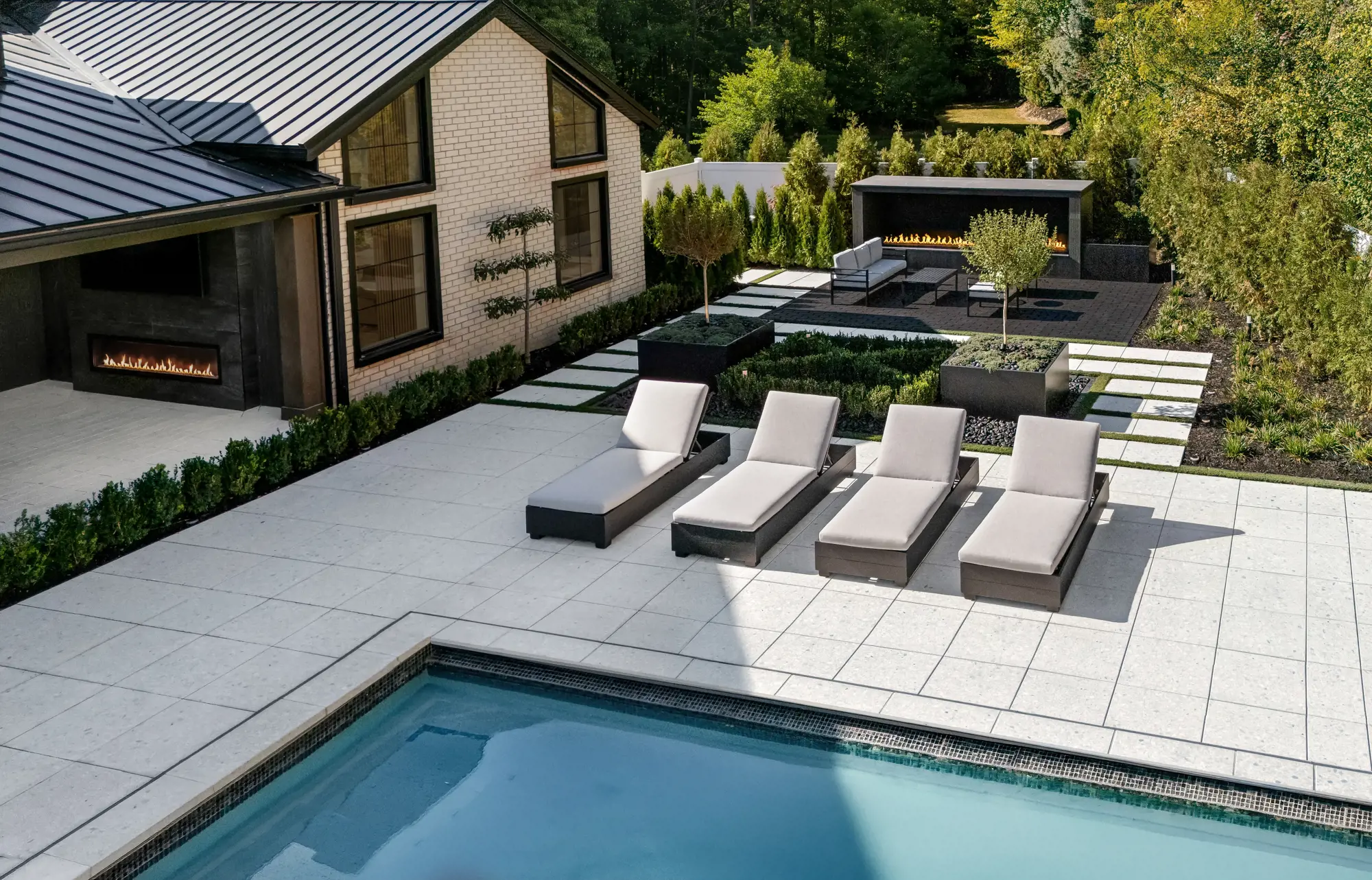 Quatre chaises longues sur dalles Terrazzo Blanc Minéral encadrées de haies de buis et de jardinières