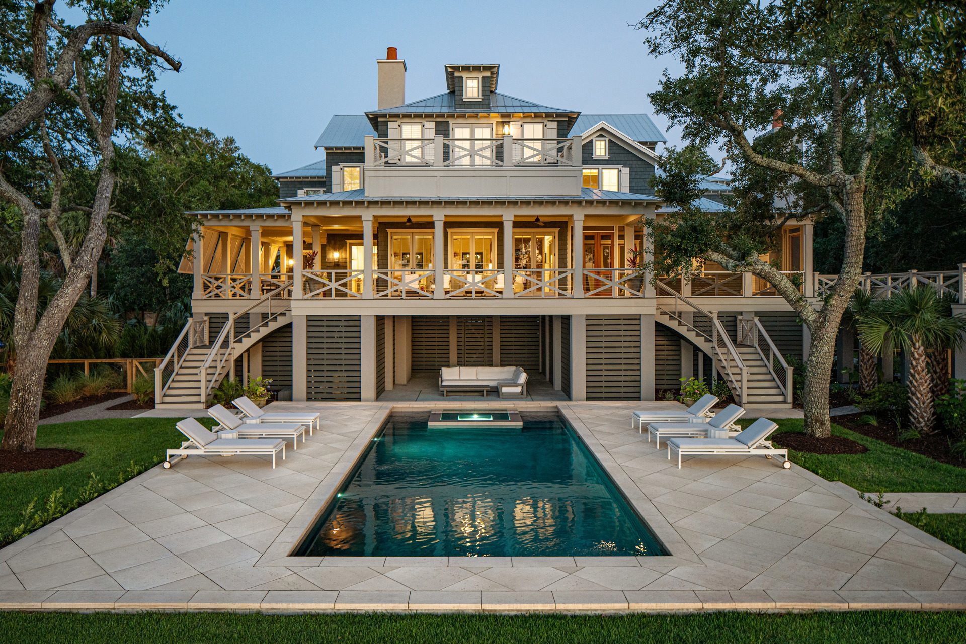 View of a large house and its backyard featuring a rectangular pool and paved patio seating area. 