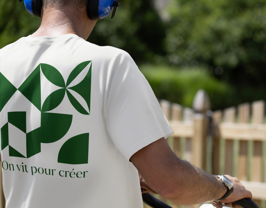 Back view of a person wearing a white co-branded Techo-Bloc t-shirt with a bold green geometric design and the phrase “We live to create.”