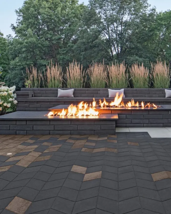 Elegant patio with Techo-Bloc Diamond pavers in dark tones around fire feature and tall grasses.