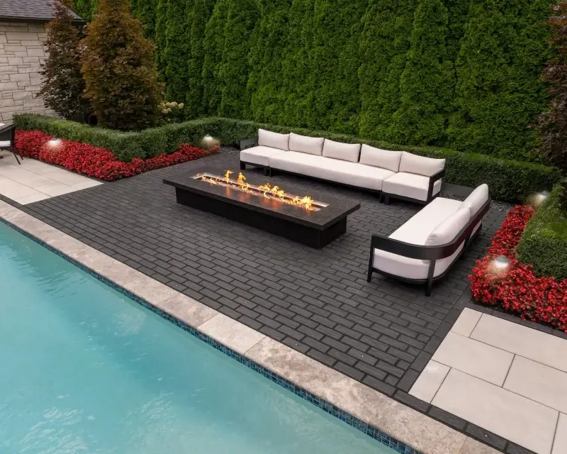 Salon extérieur moderne avec foyer sur des pavés Mika de Techo-Bloc, adjacent à une piscine et entouré de verdure et de mobilier contemporain.