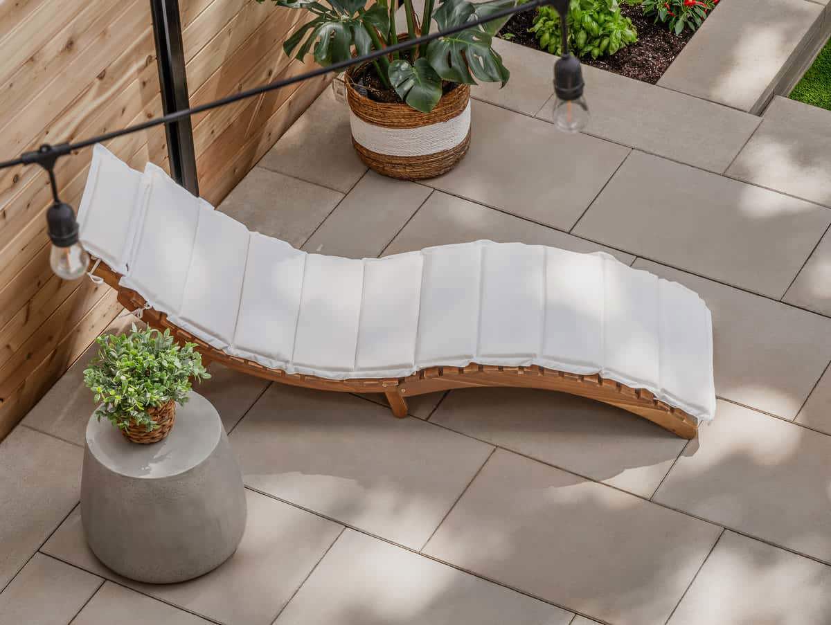 A chair with a white cushion and a wood frame on a patio of beige rectangular pavers.
