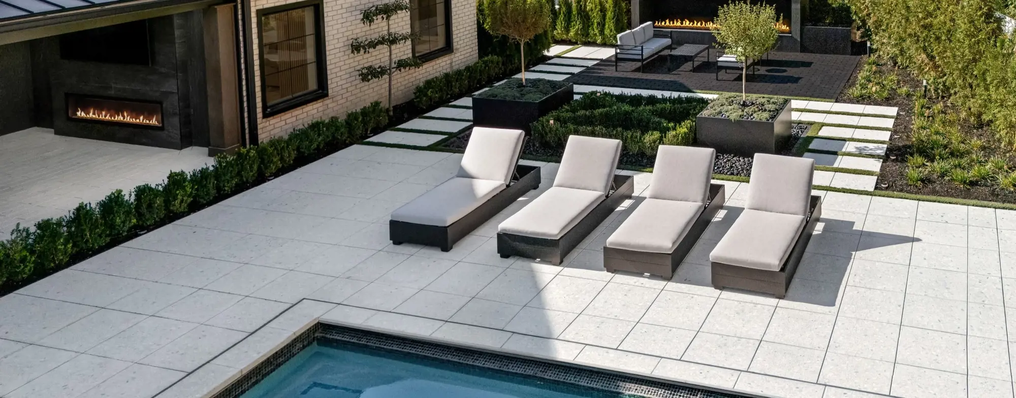 Minimalist poolside patio with Terrazzo concrete slabs, Mika pavers, and contemporary lounge seating.
