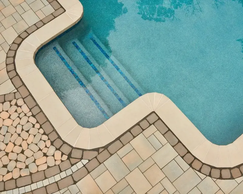 Terrasse de piscine élégante en pavés Villagio de Techo-Bloc, aux tons terre chaleureux et bords arrondis, offrant une surface antidérapante pour un style intemporel et sécuritaire.