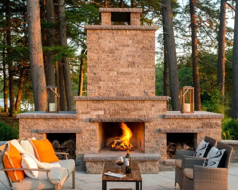 Mini-Creta outdoor fireplace in split-stone texture with seating area surrounded by trees.