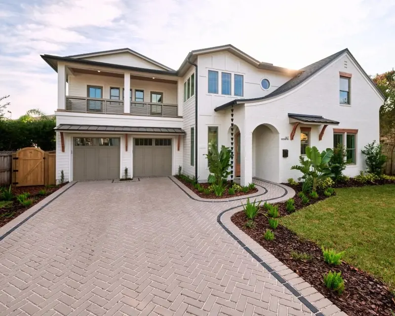 Maison moderne à deux étages avec une large allée en pavés Techo-Bloc posés en motif chevrons, bordée de plates-bandes courbées et d’un aménagement paysager verdoyant.