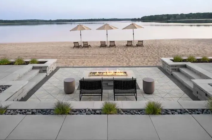 Close up view of an outdoor seating area featuring a sunken firepit, pool and patio chairs.