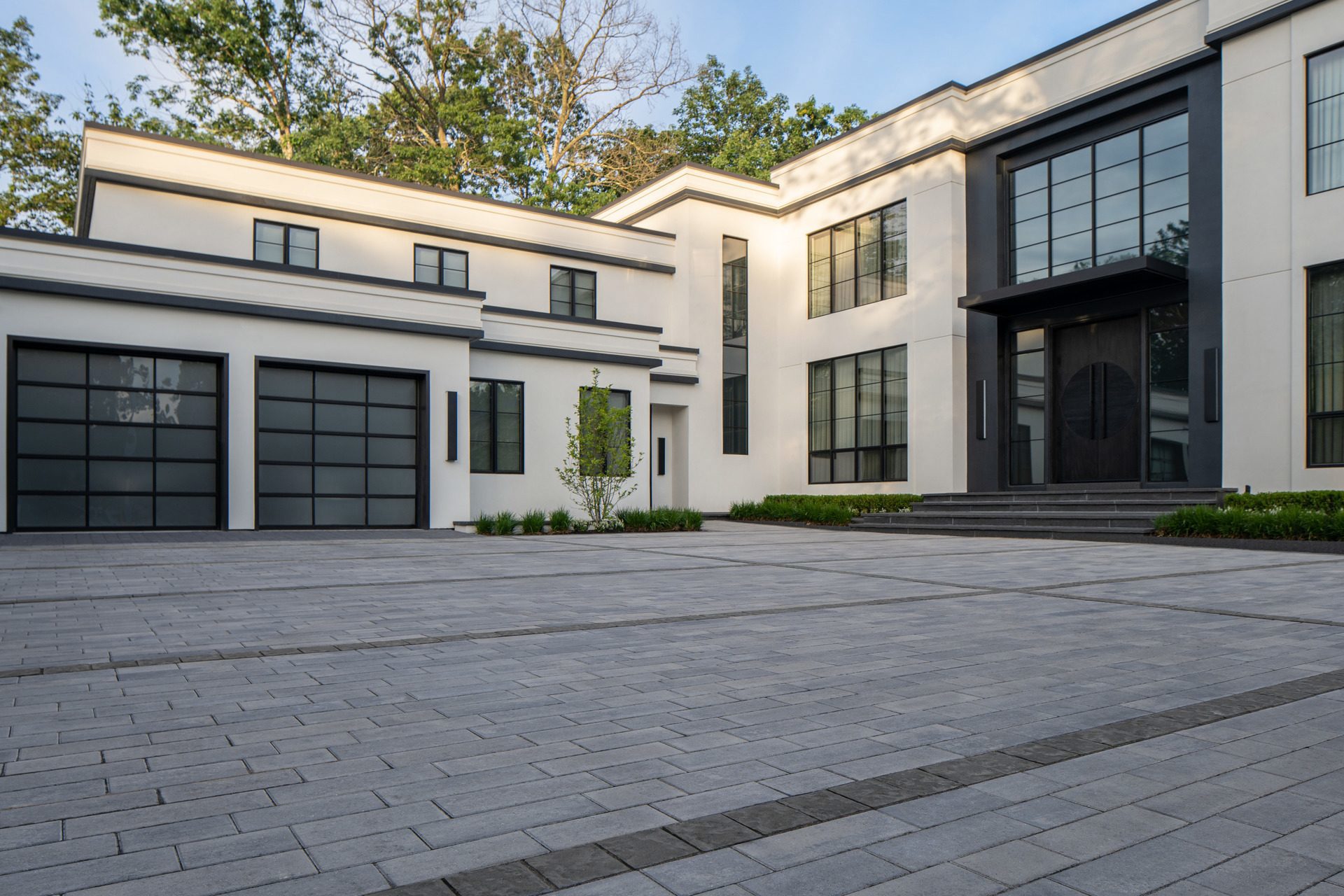 A driveway featuring grey driveway pavers with dark grey paver accents that form a linear design in front of a modern house. 
