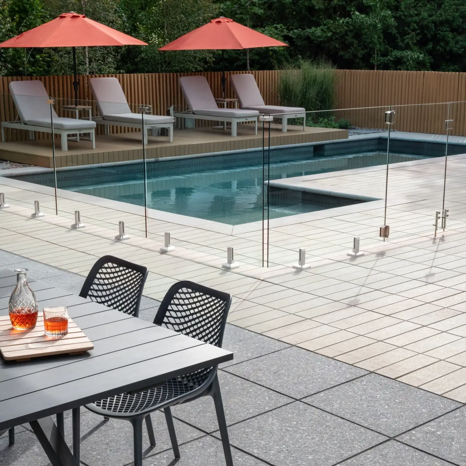 Poolside terrace featuring Terrazzo Meteor Black slabs, Greyed Nickel Industria Smooth Pavers, glass railing, and a sculptural firepit creating a refined high-contrast outdoor design.
