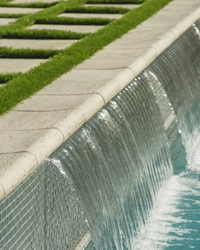 Pool waterfall edge featuring Bali Travertina Raw Caps with water flowing into a modern swimming pool. 