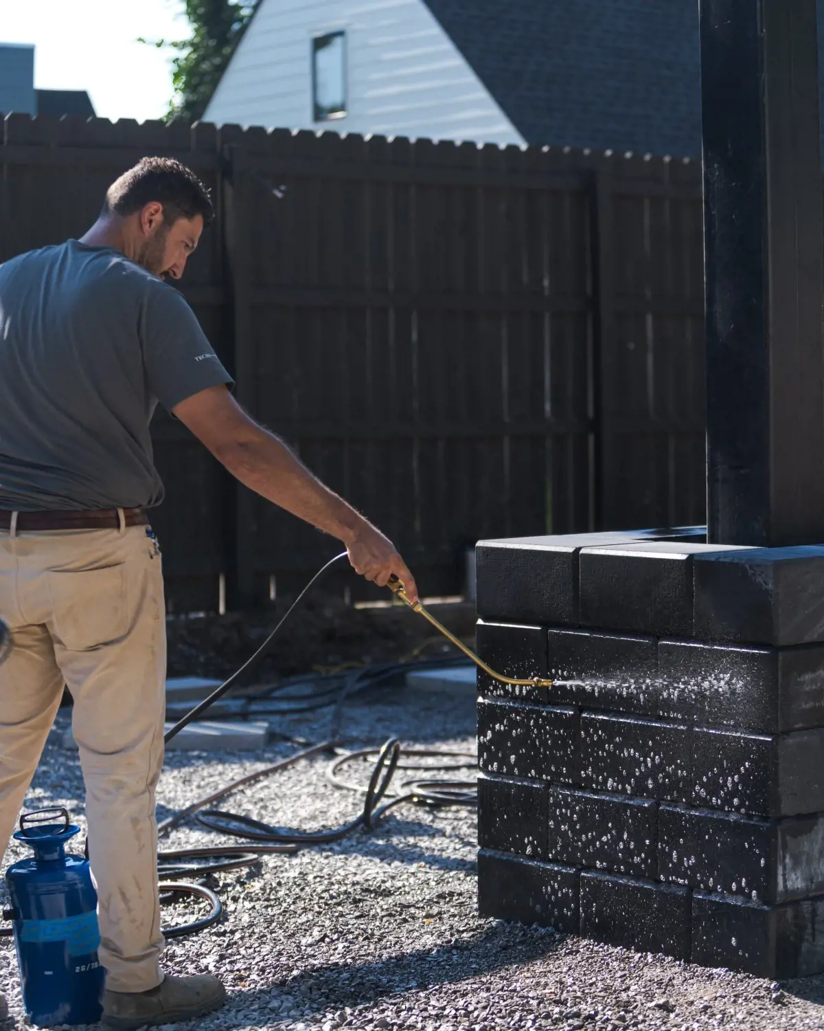 Contractor spraying cleaning or sealing solution onto stacked retaining wall blocks at a job site.