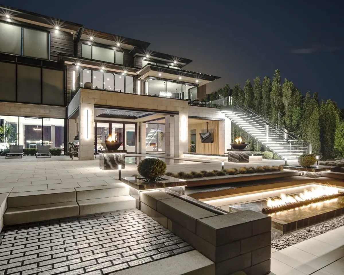 Cour arrière contemporaine avec terrasses en paliers, foyers intégrés et éclairage extérieur BOLD pour une ambiance saisissante en soirée.