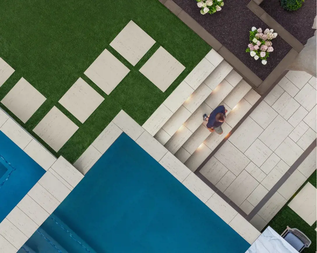 Vue aérienne d'une cour arrière moderne avec dalles en béton de couleur claire, pas japonais intégrés dans du gazon artificiel, éclairage intégré dans les marches, jardinières surélevées et piscine de luxe.