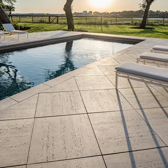 Travertina Raw Slabs by Techo-Bloc, featuring a natural travertine appearance, laid around a pool to create an elegant and durable patio with concrete strength.