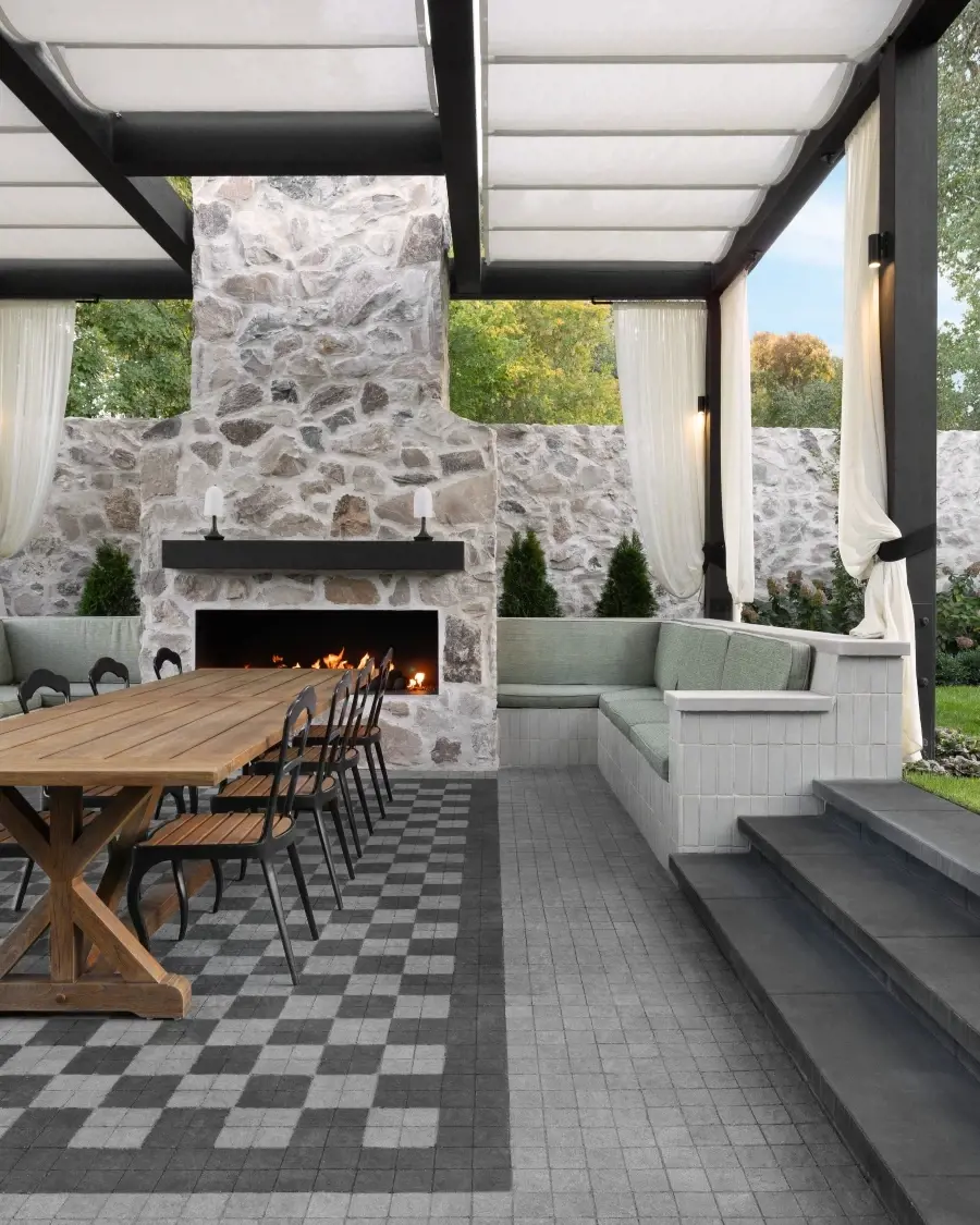 Covered outdoor dining area with a stone fireplace, patterned flooring, and layered textures that bring warmth and soul to modern design.