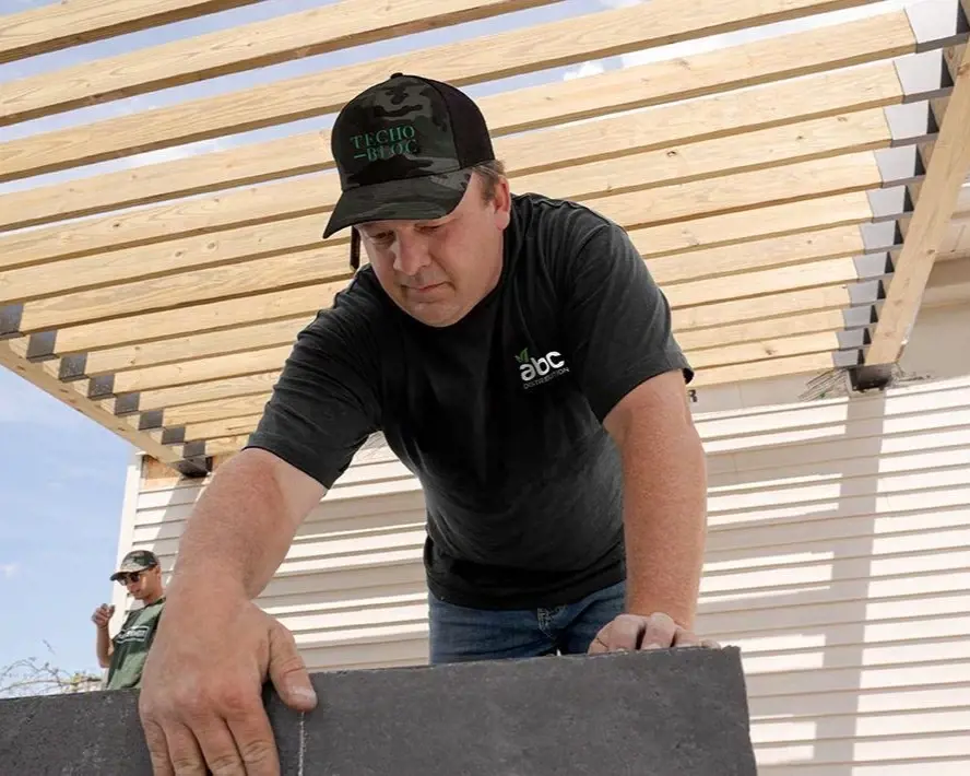 Contractor in a Techo-Bloc cap installing a large patio slab under a pergola.