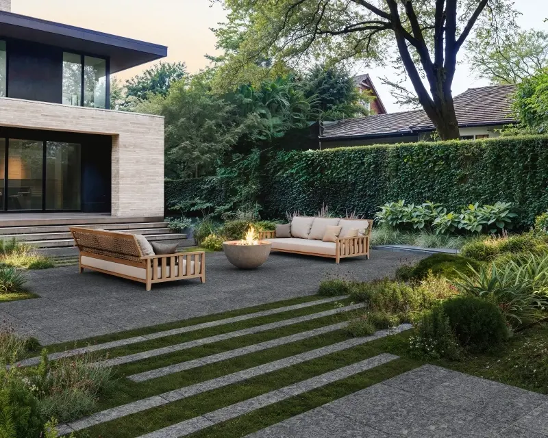 Terrazzo Slabs in Meteor Black create a patio lounge with large-format paving stones, seating, greenery, and a fire feature.