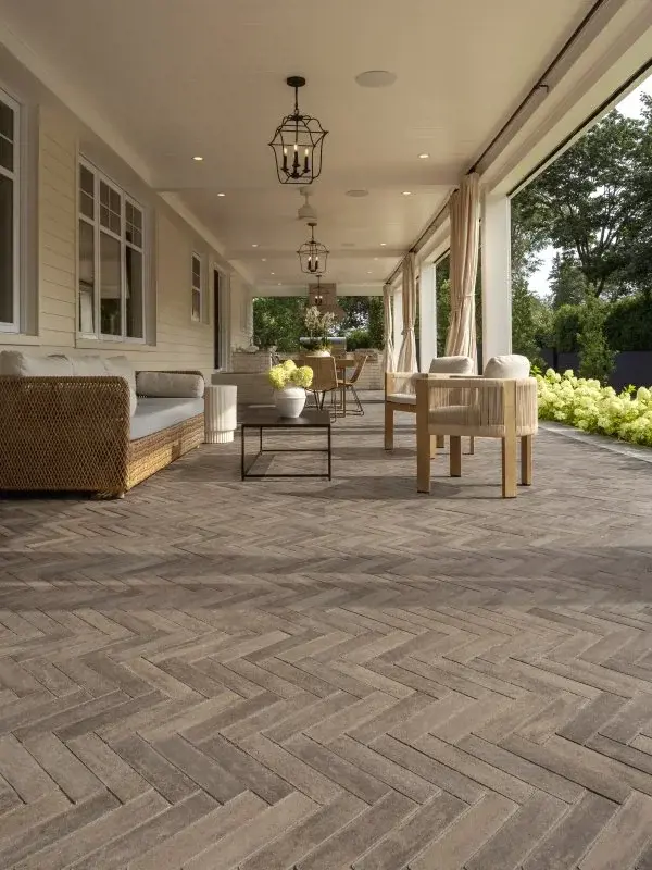 Terrasse couverte évoquant le style colonial réinventé, avec pavés en chevrons, lanterne suspendue et mobilier extérieur classique.