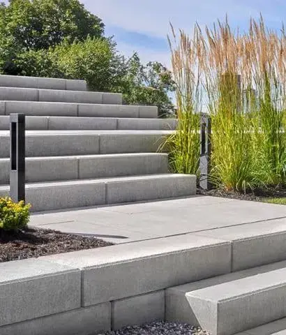 Commercial outdoor staircase built with Techo-Bloc stone steps beside ornamental grasses and modern concrete landscaping.