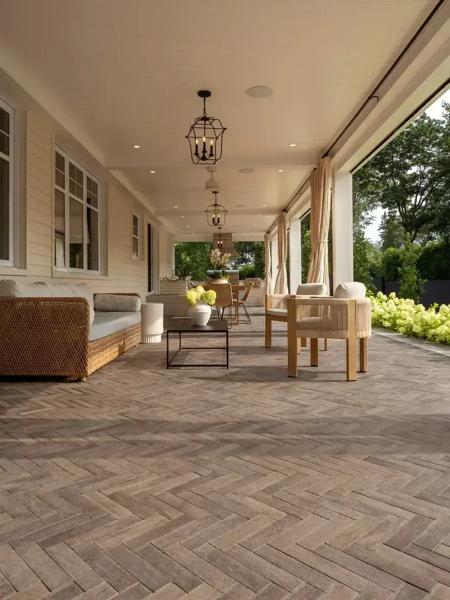 A cozy, covered patio with furniture and plants, featuring Westmount Paver in Chestnut Brown laid in a herringbone pattern.