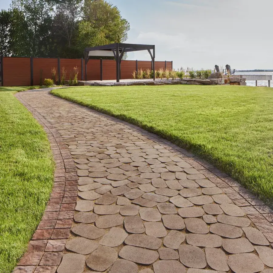 Antika Paver by Techo-Bloc in Sandlewood with irregular stone shapes, creating a rustic poolside patio with cozy lounge chairs.
