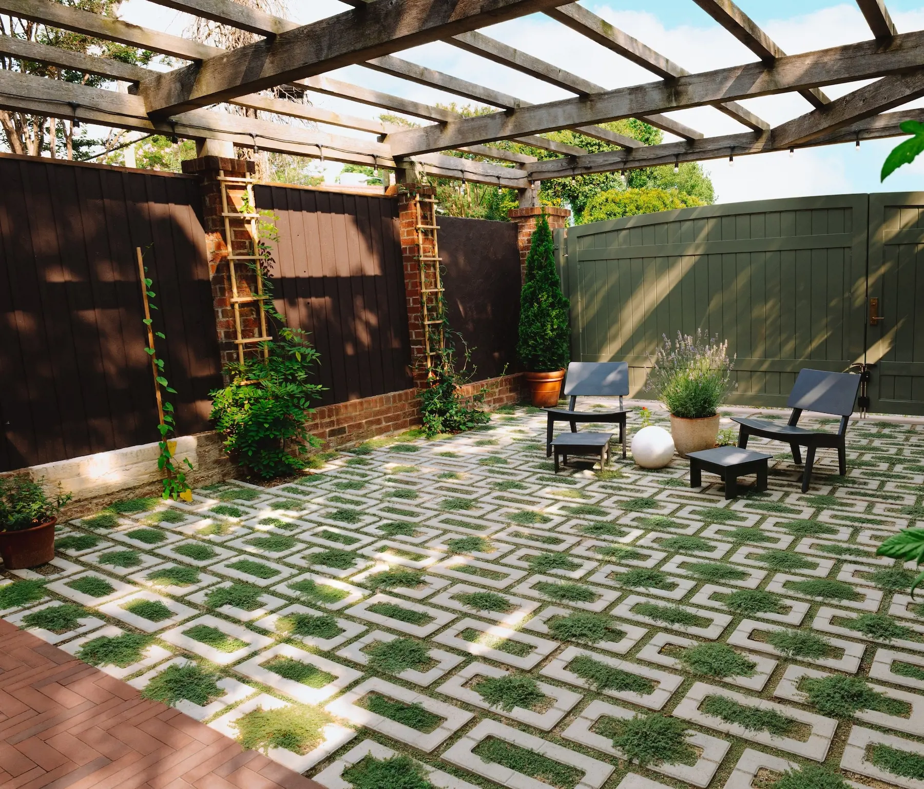 Petite cour arrière urbaine transformée avec les pavés perméables Aquastorm de Techo-Bloc, des joints engazonnés, un coin détente, des plantes grimpantes et une pergola.