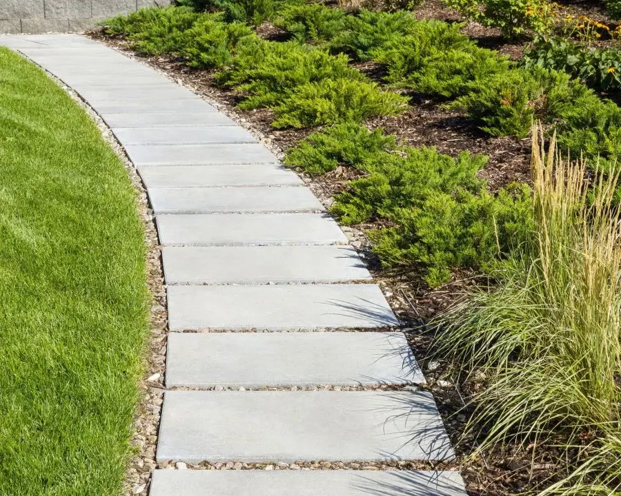 Blu 60 Smooth Slab by Techo-Bloc in Greyed Nickel, forming a curved walkway beside a manicured garden bed.