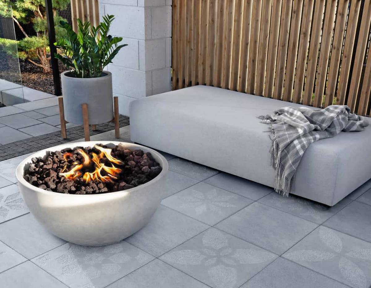 A white grey bowl serving as a firepit standing on grey pavers where light grey flower can be seen